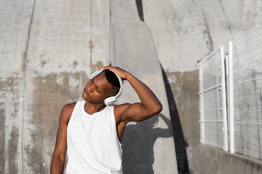 Serious African American athlete in modern headphones warming up before active running training on street - ADSF46472