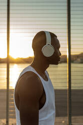 Serious African American runner listening to songs in headphones during break in active training in evening - ADSF46479