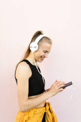 Young caucasian woman wearing headphones and sport outfit, listening to music on the phone and smiling, isolated on bright background - ADSF46489