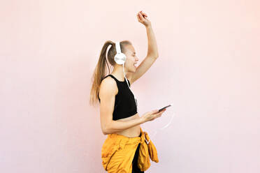 Young caucasian woman wearing headphones and sport outfit, listening to music on the phone and dancing, isolated on bright background - ADSF46490
