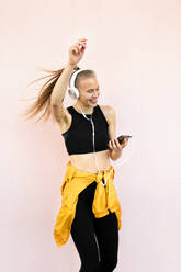 Young caucasian woman wearing headphones and sport outfit, listening to music on the phone and dancing, isolated on bright background - ADSF46500