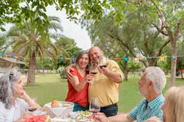 Middle aged couple hugging while celebrating occasion with friends in green park - ADSF46533