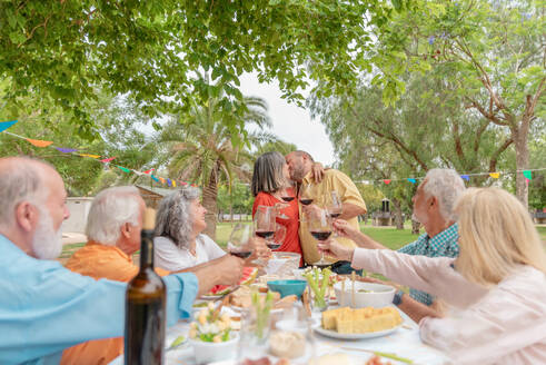 Middle aged couple hugging and kissing while celebrating occasion with friends in green park - ADSF46538