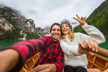 Beautiful couple of young adults visiting an alpine lake at Braies, Italy - Tourists with hiking outfit having fun on vacation during autumn foliage - Concepts about travel, lifestyle and wanderlust - DMDF01218