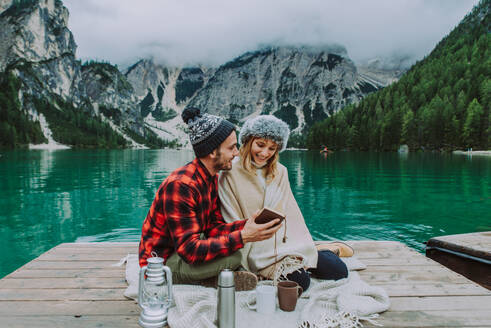 Beautiful couple of young adults visiting an alpine lake at Braies, Italy - Tourists with hiking outfit having fun on vacation during autumn foliage - Concepts about travel, lifestyle and wanderlust - DMDF01254