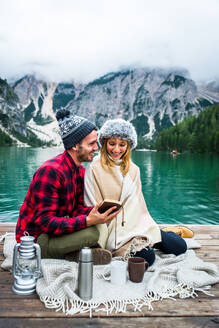 Beautiful couple of young adults visiting an alpine lake at Braies, Italy - Tourists with hiking outfit having fun on vacation during autumn foliage - Concepts about travel, lifestyle and wanderlust - DMDF01255