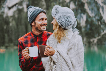 Beautiful couple of young adults visiting an alpine lake at Braies, Italy - Tourists with hiking outfit having fun on vacation during autumn foliage - Concepts about travel, lifestyle and wanderlust - DMDF01283