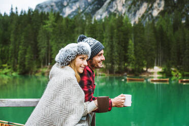 Beautiful couple of young adults visiting an alpine lake at Braies, Italy - Tourists with hiking outfit having fun on vacation during autumn foliage - Concepts about travel, lifestyle and wanderlust - DMDF01286