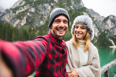 Beautiful couple of young adults visiting an alpine lake at Braies, Italy - Tourists with hiking outfit having fun on vacation during autumn foliage - Concepts about travel, lifestyle and wanderlust - DMDF01290