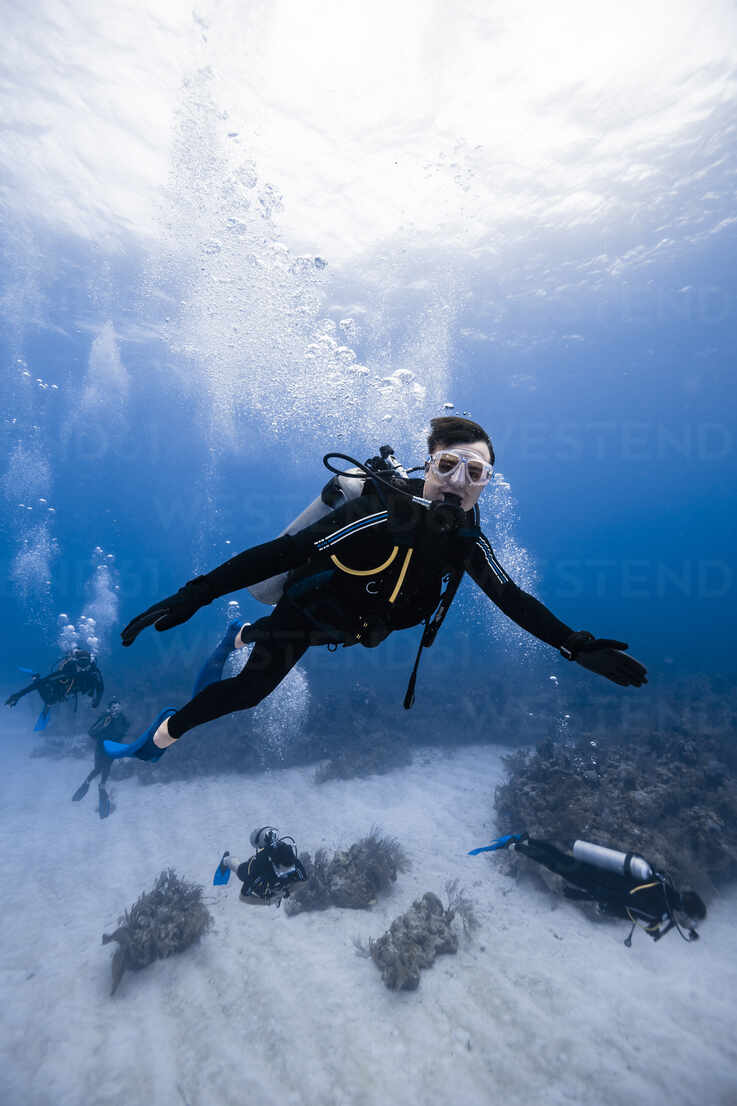 Side view of scuba diver swimming underwater with bubbles while exploring  deep clear sea during diving tour in Cancun against blurred divers stock  photo
