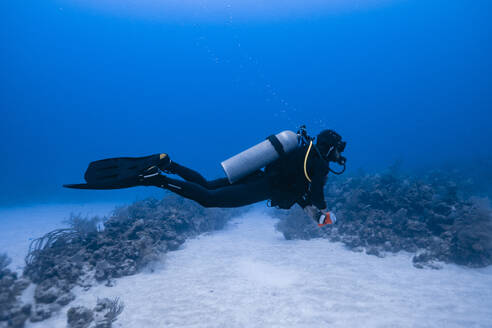 Side view of scuba diver swimming underwater with bubbles while exploring deep clear sea during diving tour in Cancun - ADSF46558