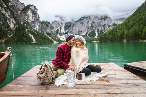 Beautiful couple of young adults visiting an alpine lake at Braies, Italy - Tourists with hiking outfit having fun on vacation during autumn foliage - Concepts about travel, lifestyle and wanderlust - DMDF01315