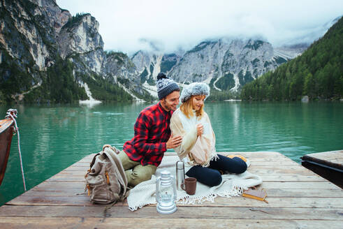 Beautiful couple of young adults visiting an alpine lake at Braies, Italy - Tourists with hiking outfit having fun on vacation during autumn foliage - Concepts about travel, lifestyle and wanderlust - DMDF01316