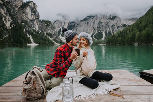 Beautiful couple of young adults visiting an alpine lake at Braies, Italy - Tourists with hiking outfit having fun on vacation during autumn foliage - Concepts about travel, lifestyle and wanderlust - DMDF01317