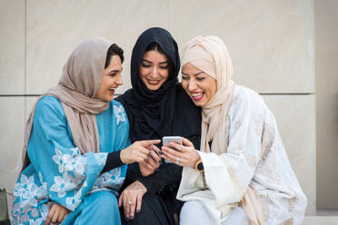 Arabische Frauen mit Abaya, die sich treffen und Spaß im Freien haben - Glückliche mittelöstliche Freunde, die sich beim Einkaufen treffen und unterhalten - DMDF01466