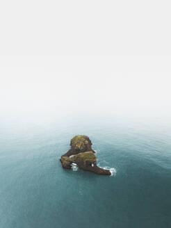 Aerial view of a rock in the ocean alogn the coastline with fog, Iceland. - AAEF19810
