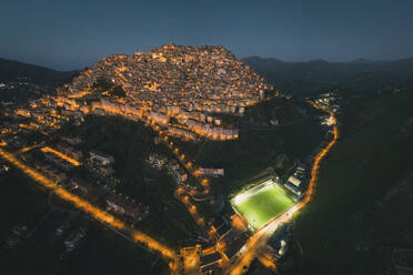 Panoramic aerial view of houses and a soccer pitch at night, Gangi, Sicily, Italy. - AAEF19854