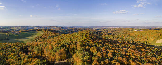 Aerial drone panoramic view of the autumn tree colors as the sun sets on the border of Burgenland and Styria in Austria under scattered clouds. - AAEF20042