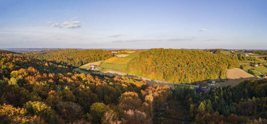 An aerial drone panoramic view of the autumn tree colors as the sun sets on the border of Burgenland and Styria in Austria under scattered clouds. - AAEF20043