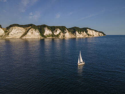 Aerial view of sailboat on a clear and sunny morning near the white Mons Klint cliffs, Denmark. - AAEF20107