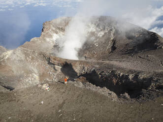 Aerial view of a person standing and looking over ledge of Gamalama volcano in Ternate, Indonesia. - AAEF20112