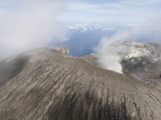 Aerial view of a person standing and looking over ledge of Gamalama volcano in Ternate, Indonesia. - AAEF20113