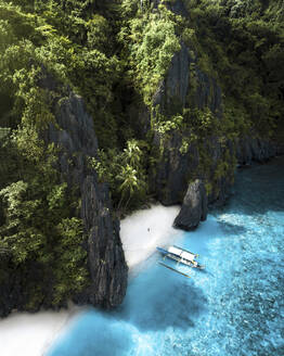 Aerial view of a person on a small beach along the wild coast with coastline and a catamaran docked at Entalula Island, El Nido, Palawan, Philippines. - AAEF20182