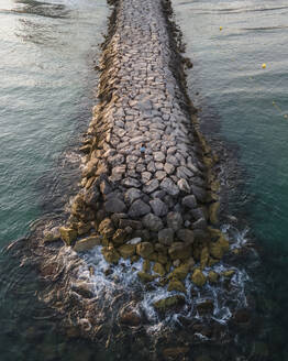 Aerial view of a woman on the breakwater at sunset along the Mediterranean Sea coastline, Sitges, Barcelona, Spain. - AAEF20382