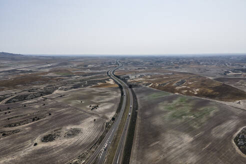 Aerial view of the highway crossing the desert valley near Monegros desert, Zaragoza, Spain. - AAEF20539