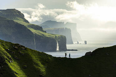 Silhouette of hikers admiring cliffs standing on top of mountain ridge above the ocean, Kalsoy island, Faroe Islands, Denmark, Europe - RHPLF26086