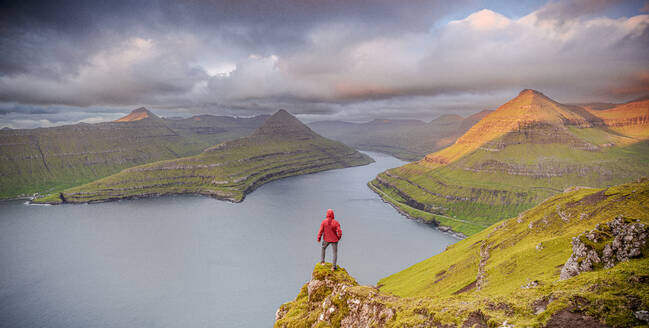 One man contemplating the sky at dawn standing on rocks above a fjord, Eysturoy Island, Faroe Islands, Denmark, Europe - RHPLF26087