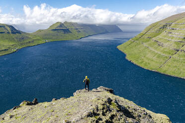 High angle view of hiker admiring mountains and ocean standing on top of a mountain, Klaksvik, Bordoy Island, Faroe Islands, Denmark, Europe - RHPLF26094