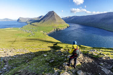 Hiker standing on top of hill with Vidareidi village and Malinsfjall mountain on background, Vidoy Island, Faroe Islands, Denmark, Europe - RHPLF26097