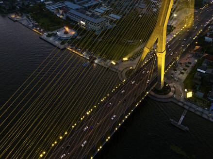 Aerial view of The Rama VIII Bridge, a cable-stayed bridge crossing the Chao Phraya River at night in Bangkok, Thailand. - AAEF20863