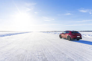 Side view of a red car travelling on empty icy road on the frozen sea, Lulea, Norrbotten County, Lapland, Sweden, Scandinavia, Eurupe - RHPLF26517