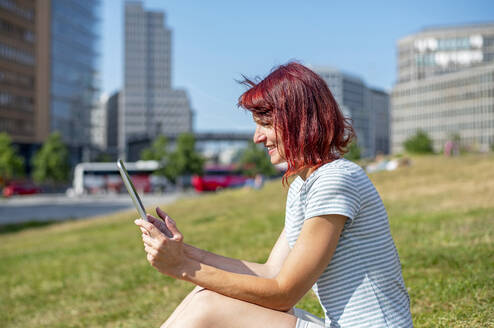Smiling woman using tablet PC sitting on grass - BFRF02431