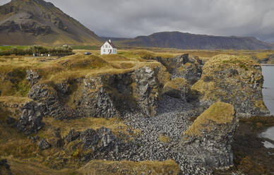 A classic view of the basalt lava cliffs on the coast at the village of Arnastapi, backed by the mountains of Snaefellsjokull, Snaefellsjokull National Park, Snaefellsness peninsula, west coast of Iceland, Polar Regions - RHPLF26697