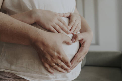 Daughter and mother making heart shape with hand on abdomen - OSF01948