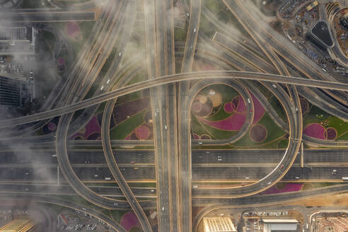 Aerial view of vehicles driving a complex road intersection in Dubai downtown with low clouds fog, United Arab Emirates. - AAEF21016