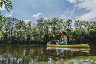 Young woman meditating on paddleboard in lake - YTF01027