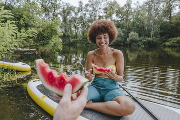 Glückliche Frau isst Wassermelone mit Freund auf Paddleboard in See - YTF01036