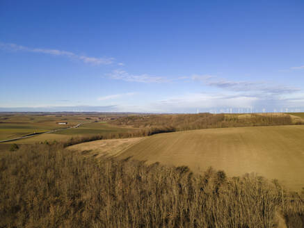 Aerial drone view in winter of agricultural fields and countryside with scattered clouds against a blue sky with wind turbines in the distance, Spannberg, Lower Austria, Austria. - AAEF21394