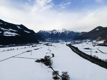 Aerial drone view of the Ziller river in the Ziller valley in winter covered in snow on a cloudy day with the peak Rofanspitze in the distance, Fuegen, Tyrol, Austria. - AAEF21395