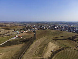 Aerial drone view in early spring of vineyards in wine country with a small town and wind turbines in the distance on a clear day, Poysdorf, Lower Austria, Austria. - AAEF21398