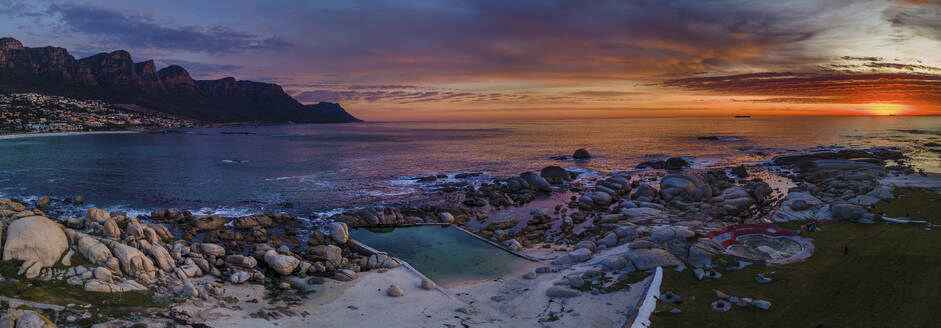 Panoramic aerial view of Maiden’s Cove Tidal Pool at dramatic sunset with Camps Bay in background, Cape Town, South Africa. - AAEF21420