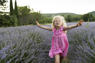 Happy girl with arms outstretched running in lavender field - SVKF01594