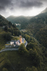 Aerial drone view on a church in Cerentino with the stone village of Corino in the background, Valmaggia, Switzerland. - AAEF21595