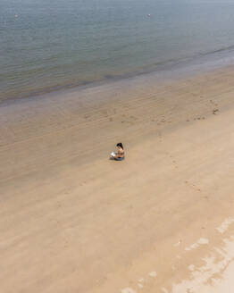 Aerial view of a person along the shoreline with a book at Baia de Sao Martinho do Porto, Leiria, Portugal. - AAEF21685