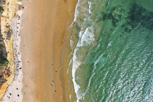 Aerial view of the blue ocean with the white waves and the brown sand with people on it in the town of Conil de la Frontera on Playa La Fontanilla in Cádiz, Andalusia, Spain. - AAEF21733