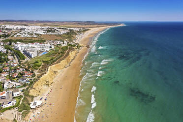 Aerial view of a coastline with cliffs, along line of white waves and turquoise waters in the town of Conil de la Frontera on the Playa La Fontanilla in Cádiz, Andalusia, Spain. - AAEF21734
